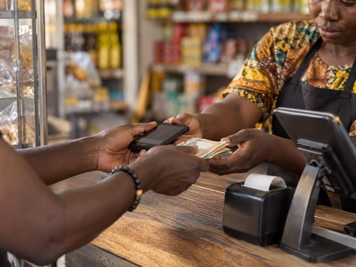 Customer handing banknotes and a phone to a cashier across a shop counter