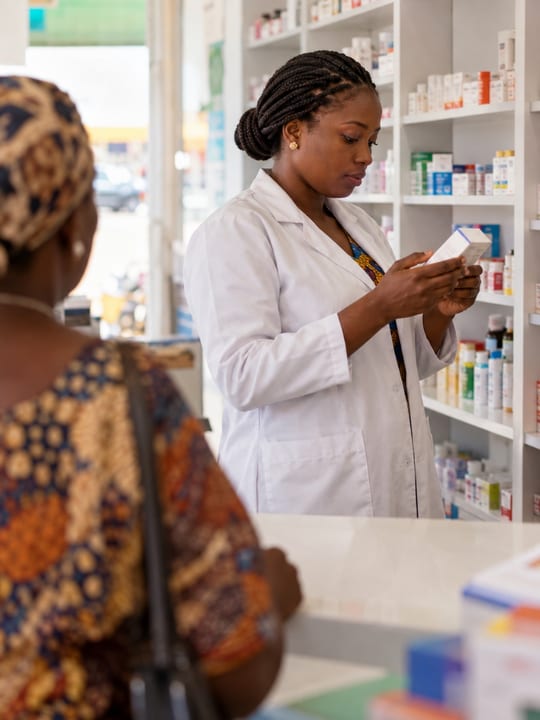 Pharmacist reading a medicine label in front of stocked shelves while a customer waits at the counter